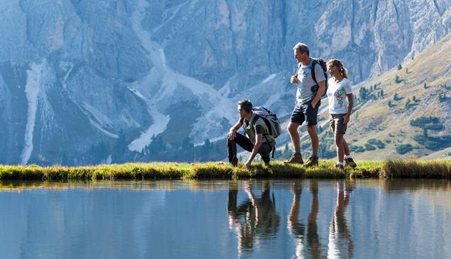 Drei Wanderer an einem See; im Hintergrund die Dolomiten.